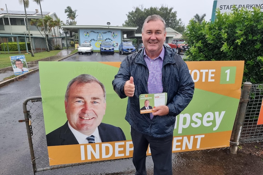 Man in a rain jacket stands in front of his core flukes giving a thumbs up 