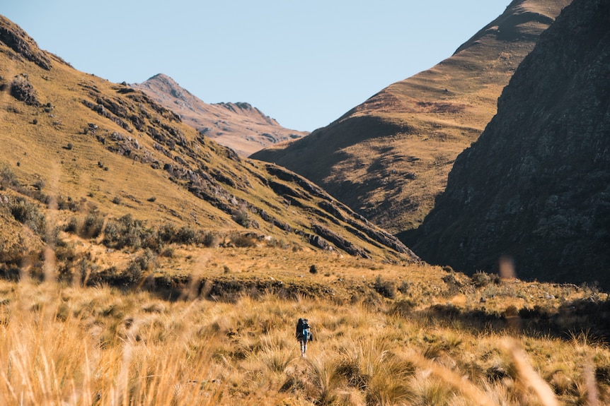 A woman can be seen walking into a vast, mountainous landscape