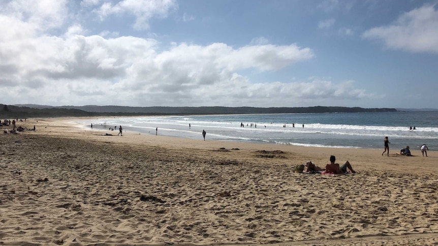 Tathra Beach with a few people walking and sunbathing.