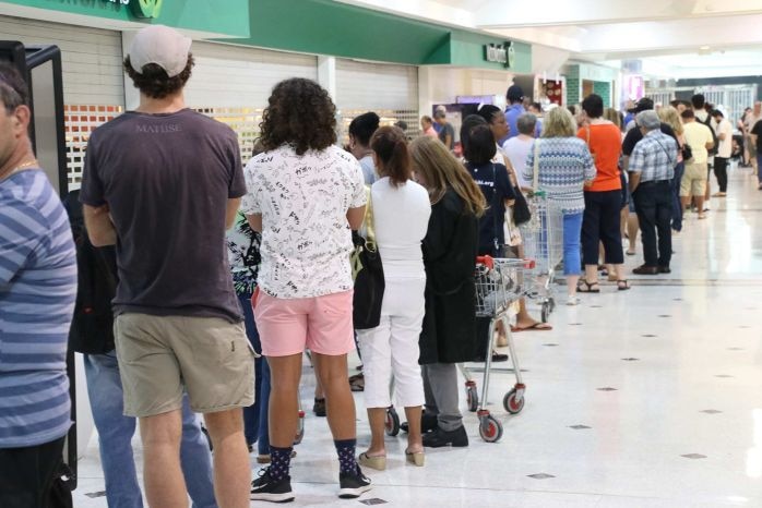 A line of about 20 stands in front of a supermarket.