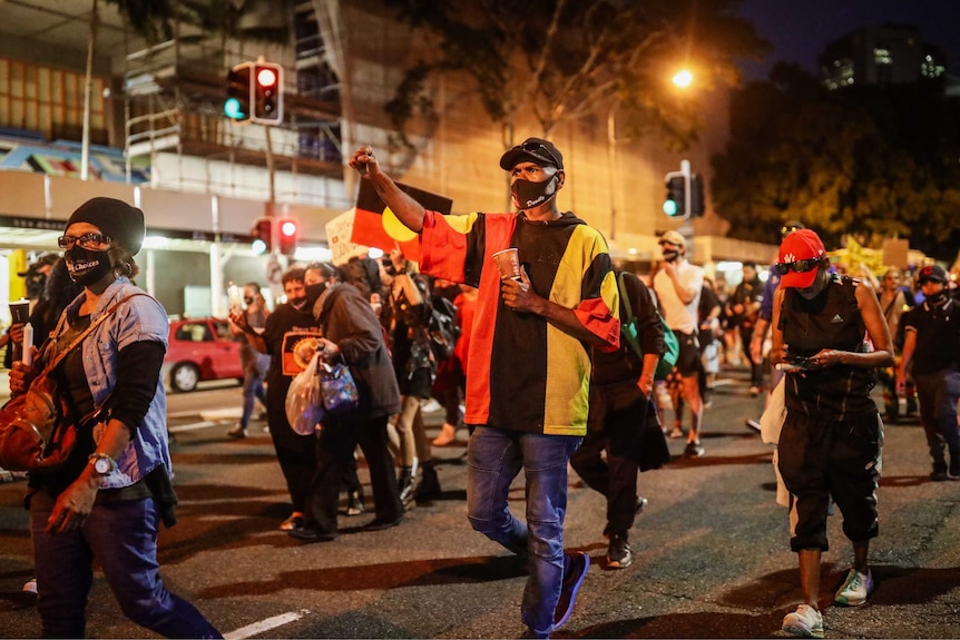 A man hold his fist in the air while walking with a group holding Aboriginal flags.