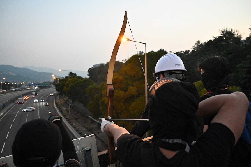 A protester with a bow aims an arrow at vehicles on a highway below.