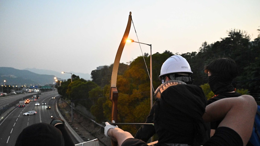 A protester with a bow aims an arrow at vehicles on a highway below.