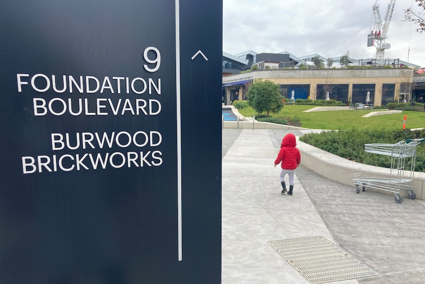 a sign out the front of Burwood Brickworks with the name of the development. It also shows part of a garden with a child in it.