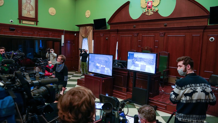 Journalists watch TV showing hearings on the liquidation a human rights group