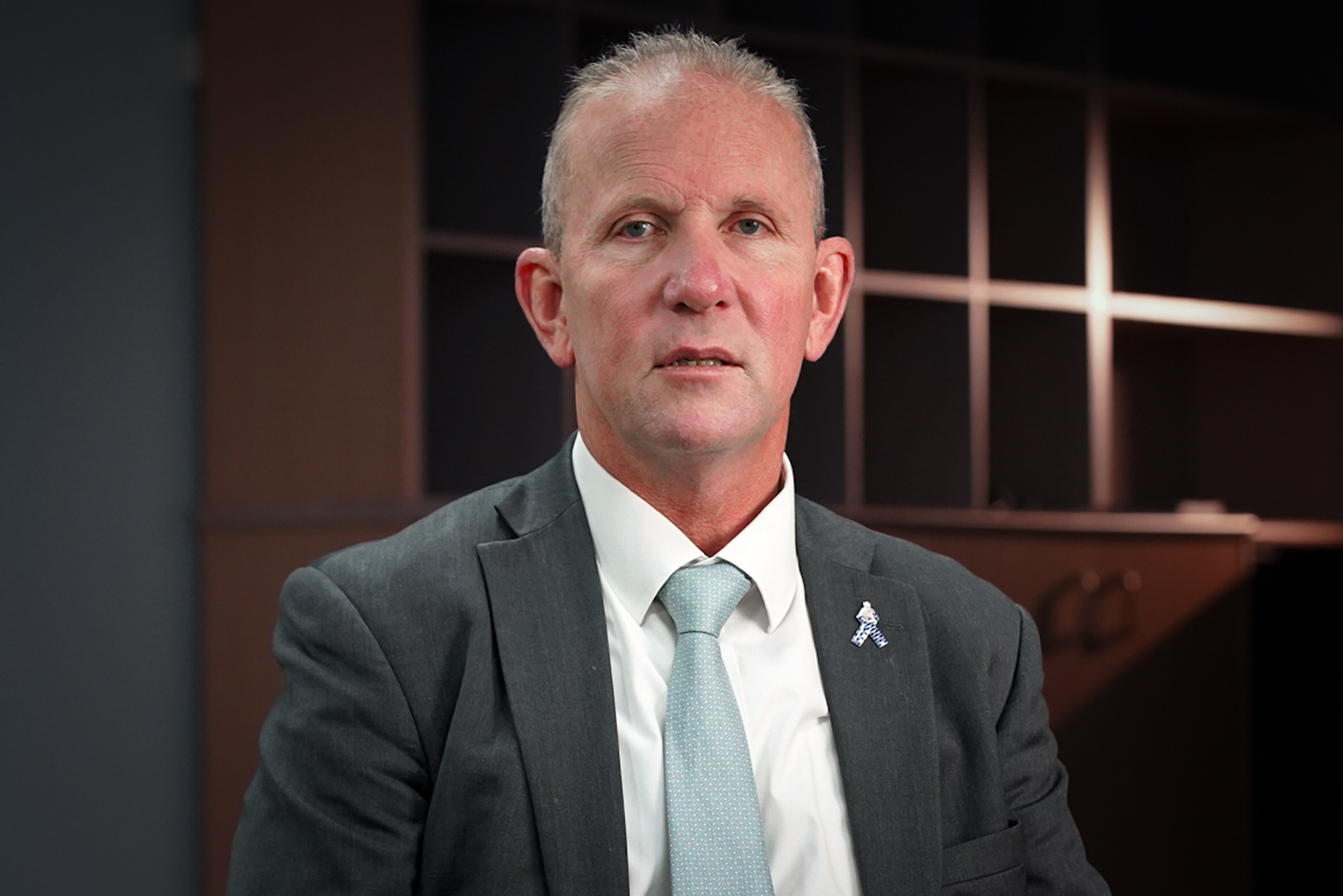 Older man in a dark grey suit with a light green tie. 