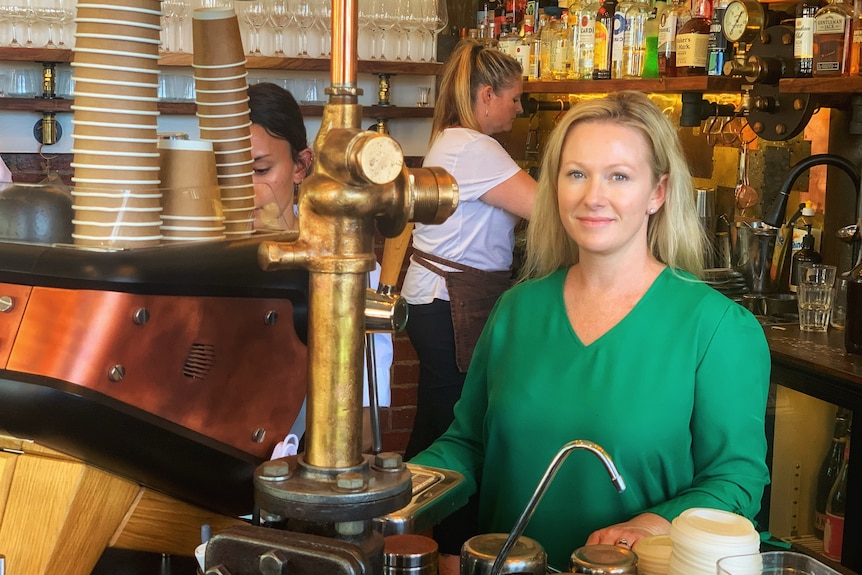 A smiling woman wearing green sits behind a beverage counter.