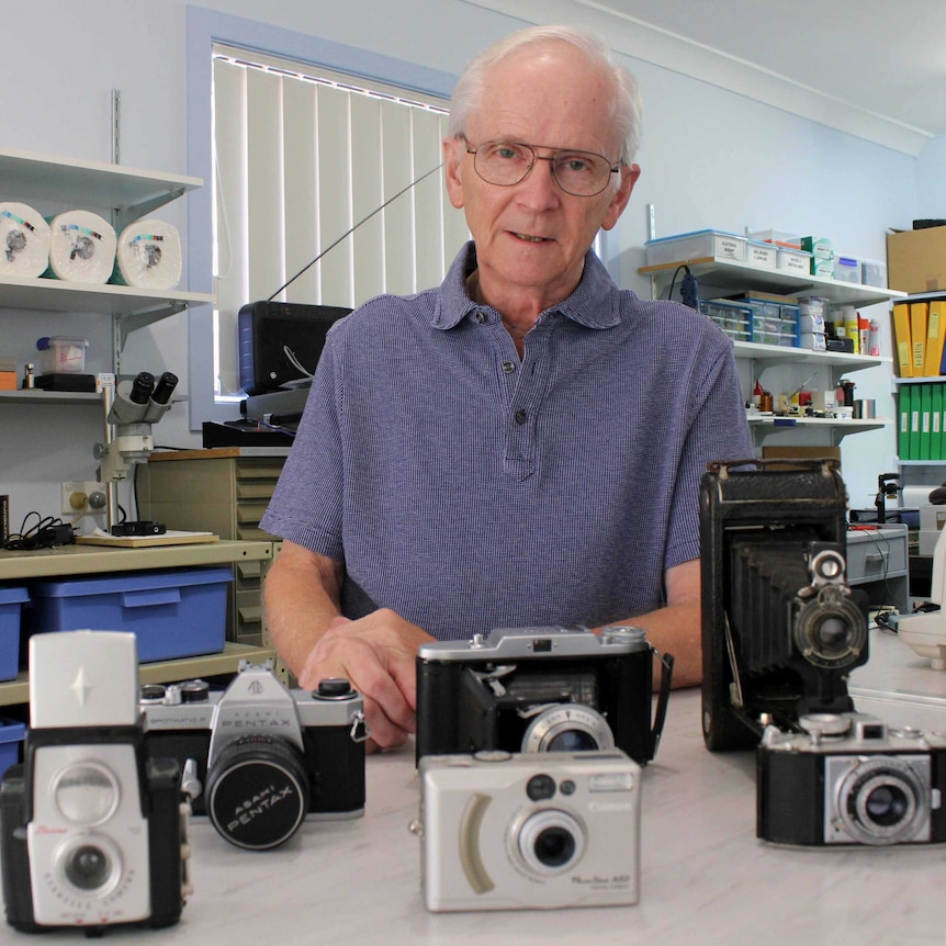 Older man in workshop with old cameras