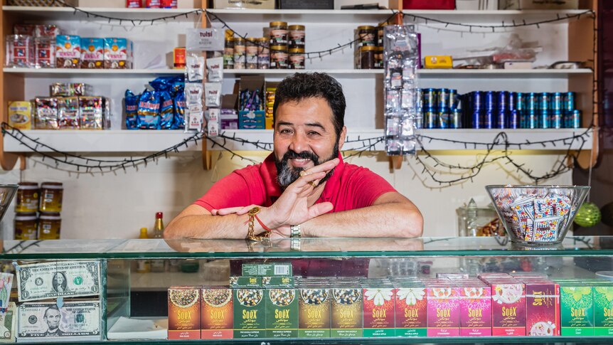 Sanjay smiles and waves in his shop, surrounded by colourful products.