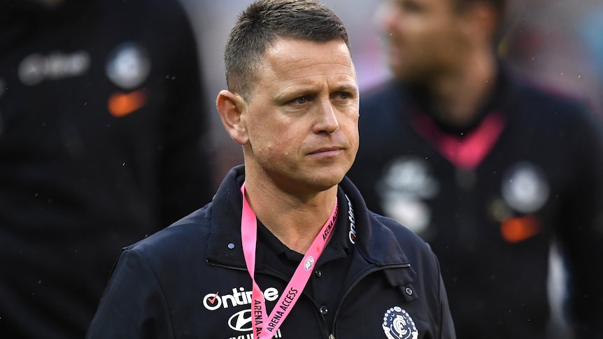 Brendon Bolton has a neutral expression on his face wearing a dark blue jacket with a lanyard around his neck