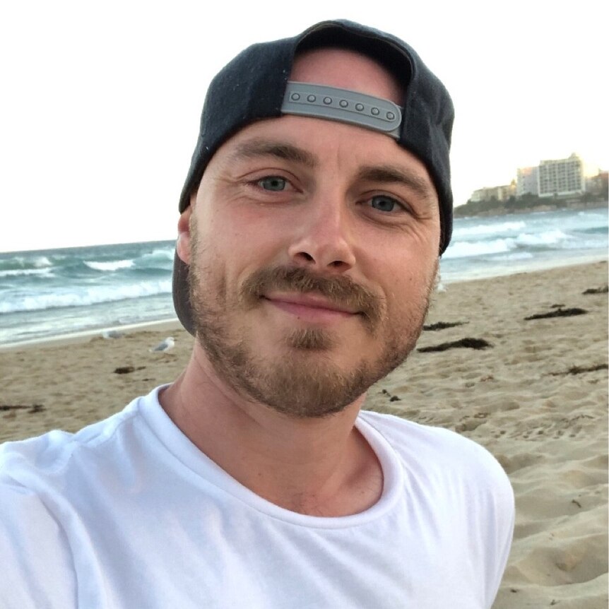 A man takes a selfie in front of a beach.