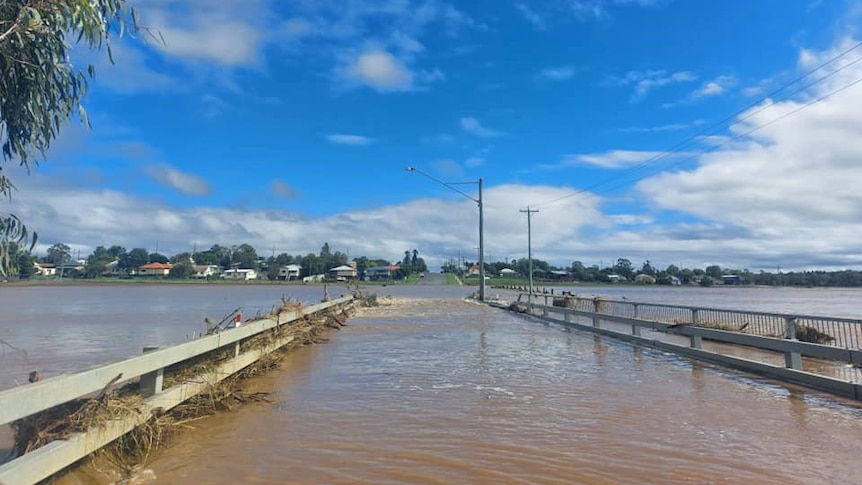 Flooded Grafton Bridge in Warwick showing water over the roadway and homes in the distance