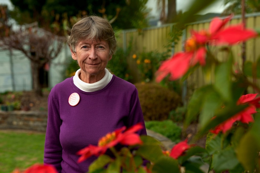 a woman in a purple top in a garden with red flowers in the foreground