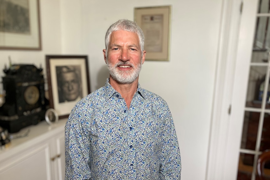 A middle-aged man with a white beard, wearing a floral shirt, smiles at the camera.