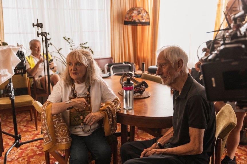 A behind the scenes look on the set of Mother and Son with Denise Scott and Geoffrey Atherden sitting on a chair near a camera