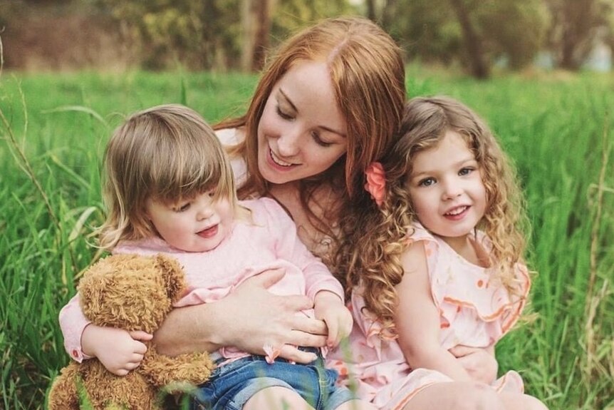 Belinda Dowde with her daughters Sylvie and Marley sitting on grass.