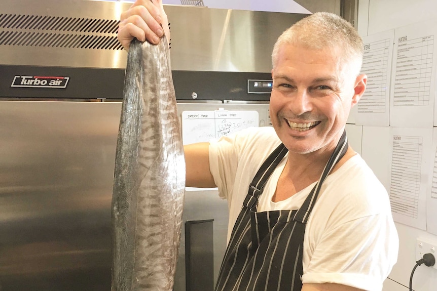 Justin Bull holds a large fish in a kitchen