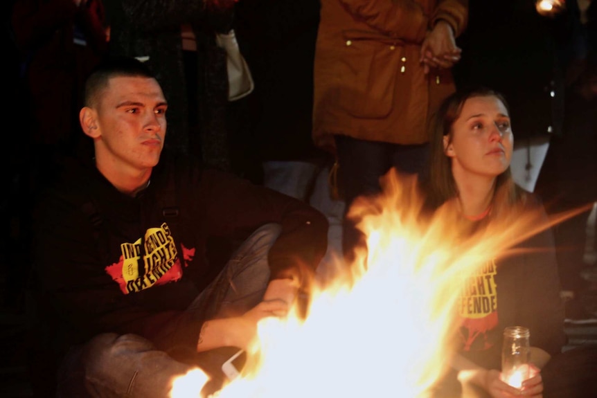 A man and a woman sit by a fire at a protest.