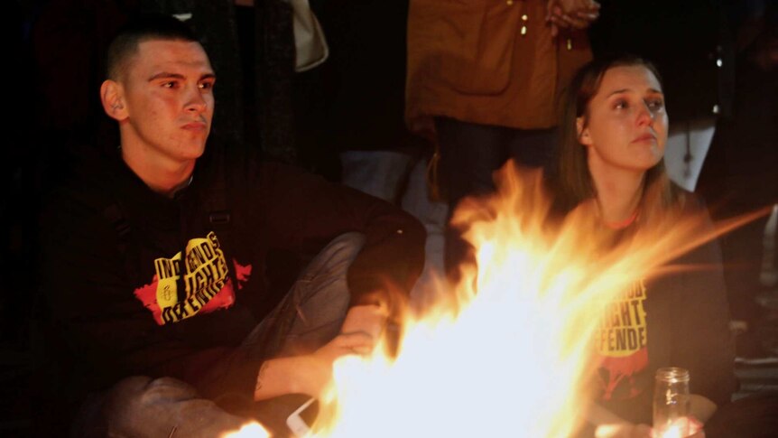 A man and a woman sit by a fire at a protest.