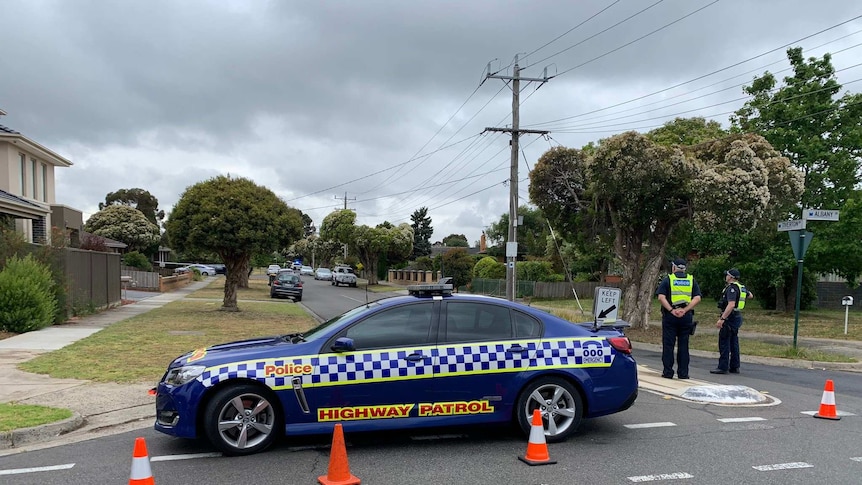 A police car and traffic cones block a residential street where two police officers stand guard.