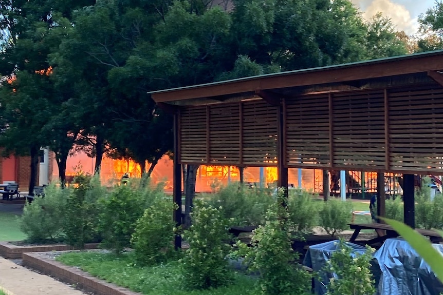 A building fire behind large trees and another building.