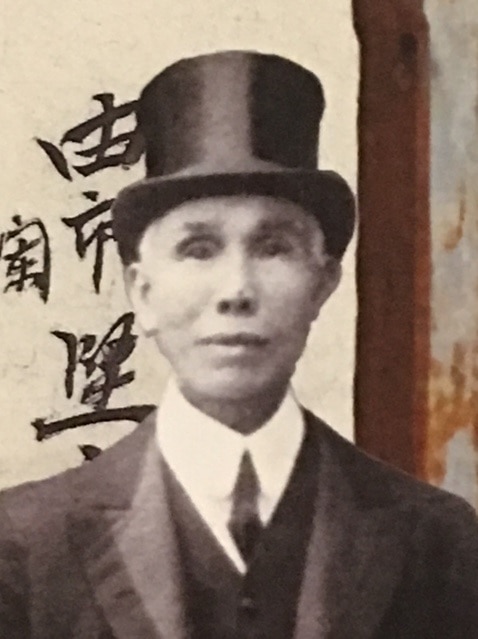 Kwong Sue Duk wears a suit and top hat and looks at the camera