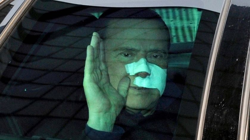 Italian Prime Minister Silvio Berlusconi waves to journalists as he leaves San Raffaele hospital
