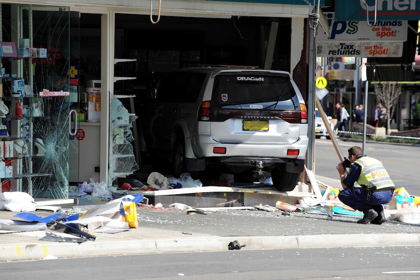 A policeman photographing a four wheel drive which crashed through the shop front of a pharmacy.