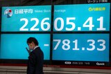A man wearing a face mask walks past a screen showing Tokyo's stock market sharply lower.
