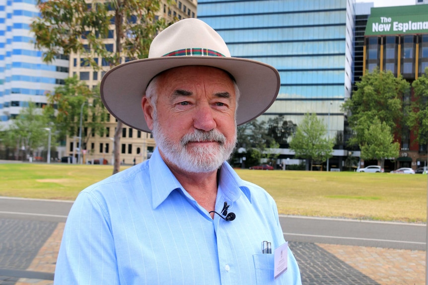 Robin Scott headshot. He wears a wide-brim hat with a city background.