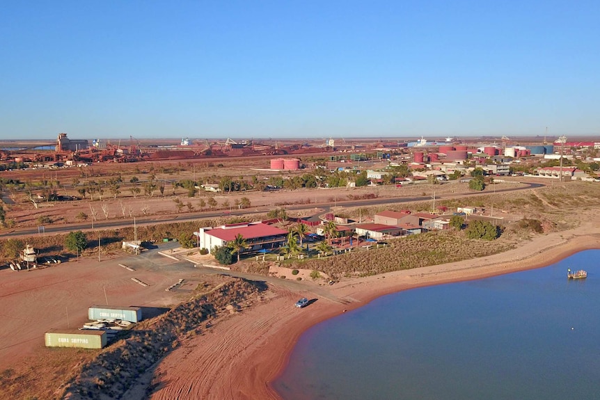 Drone footage looks back towards a coastal town and its industrial area.