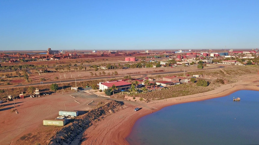 Drone footage looks back towards a coastal town and its industrial area.