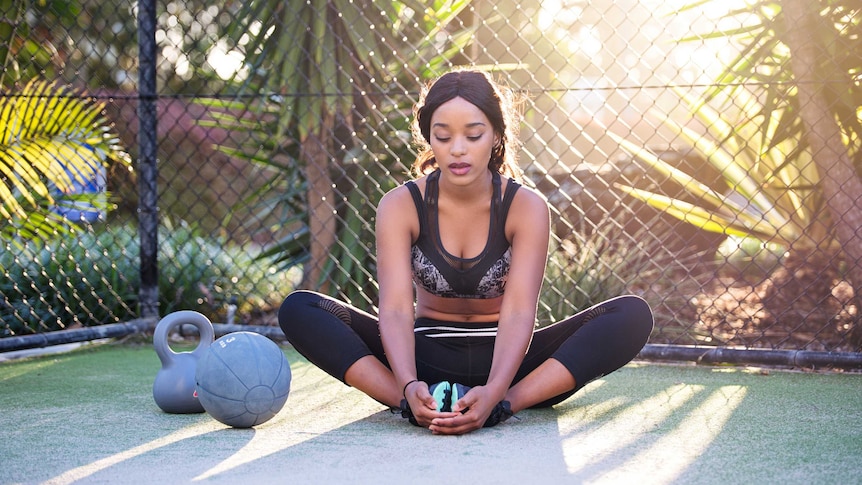 Woman sitting on tennis court with dumbbells to depict exercise equipment you don't have to spend a lot of money on.