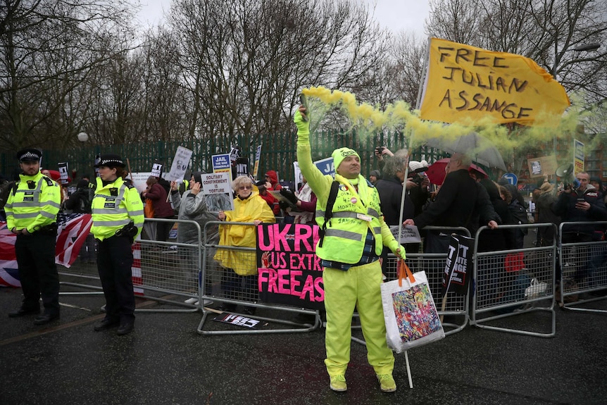 A demonstrator dressed in yellow, and holding a yellow smoke flare, stands in front of a crowd.