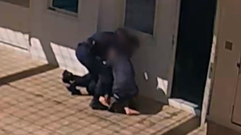 A screenshot of two uniformed officers restraining an person on the floor with their face blurred. 