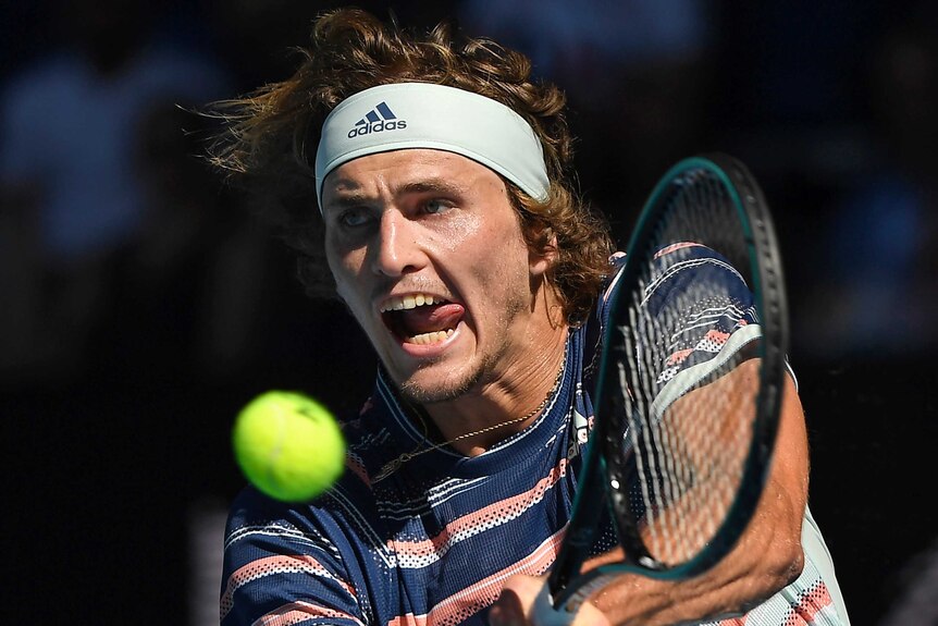 A male tennis player sticks his tongue out as he plays a backhand at the Australian Open.