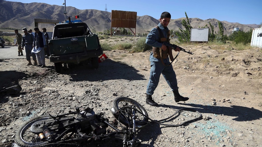Afghan police inspect the site of a suicide attack. The motorcycle the bomber used is on the ground, surrounded by rubble.