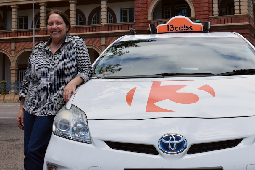 A smiling woman leans on a taxi.