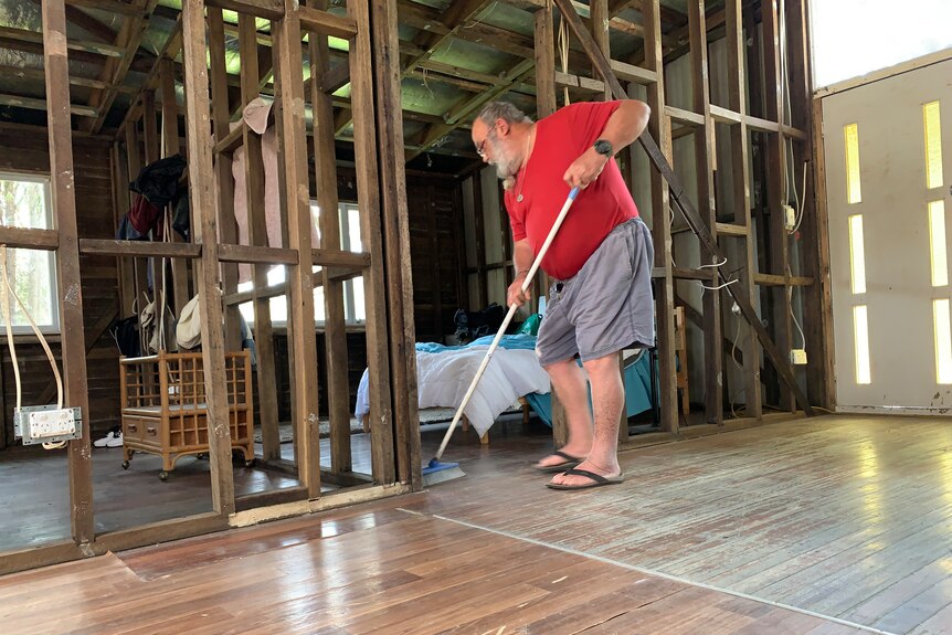Allen Kunst sweeping his in his home. The walls are just frames.