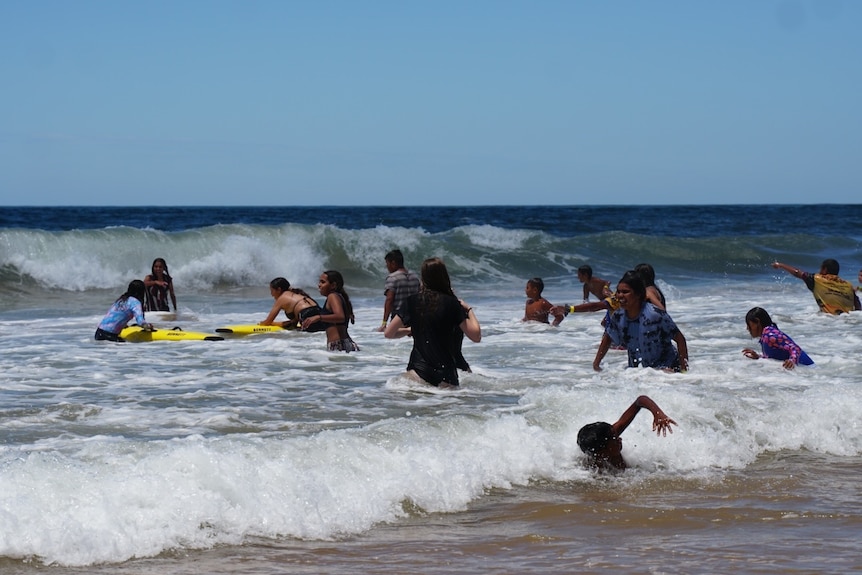 A group of Indigenous kids among the waves at a beach.