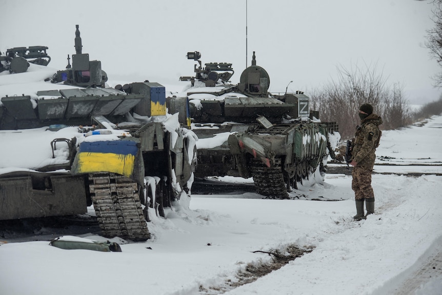 A Ukrainian serviceman stands near captured Russian tanks, one painted in the colour of the Ukrainian flag