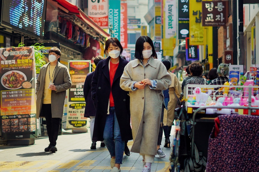 Two Korean women in face masks walk through a busy Seoul laneway 