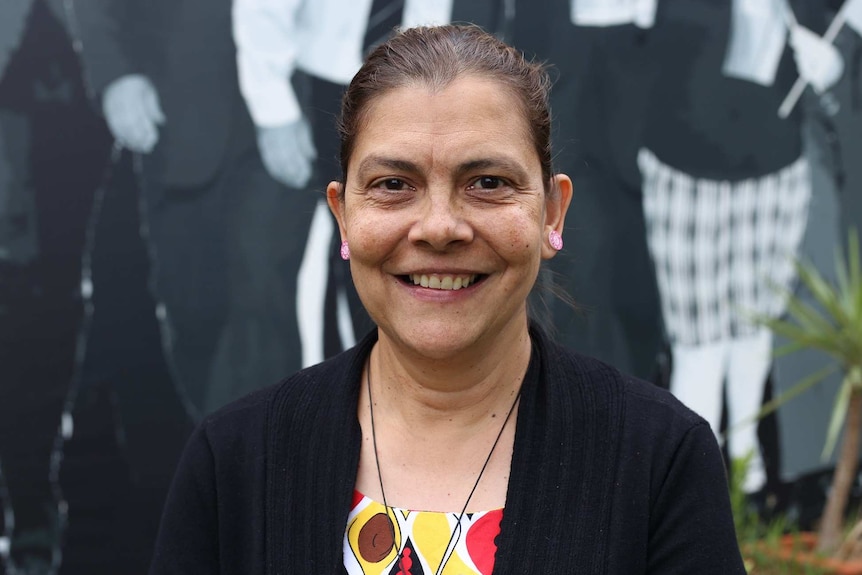 Tracey Evans smiles as she stands in front of a mural of past Aboriginal leaders.