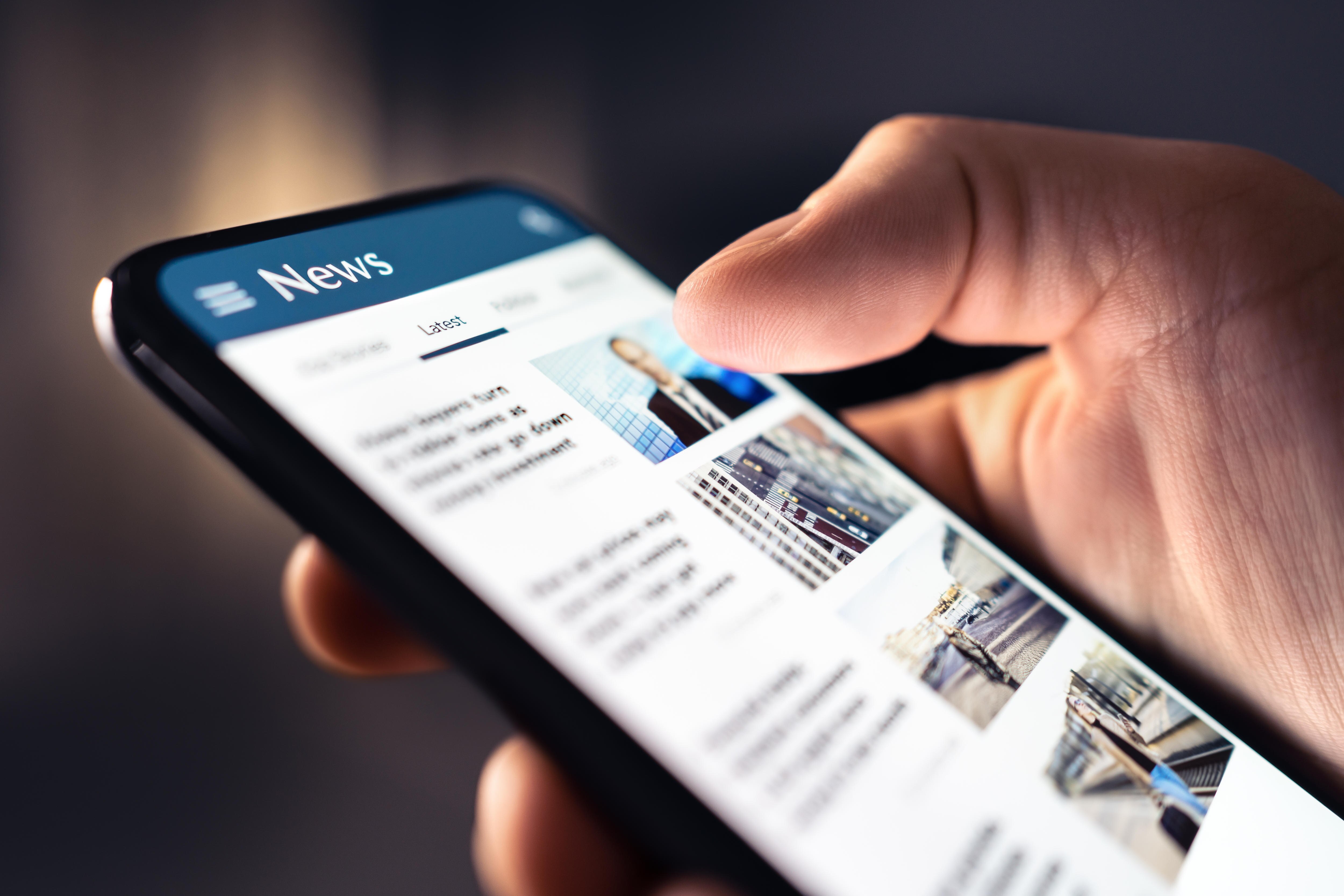 A close-up of hand scrolling through the news on a phone