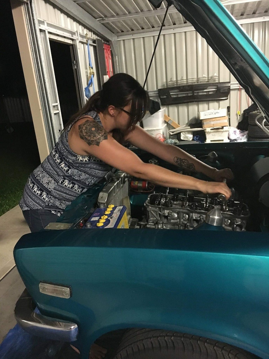 Girl in singlet works under the bonnet of a classic green car