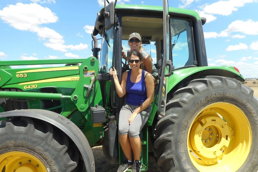 Two young farm workers pose for a photo inside a farm tractor.