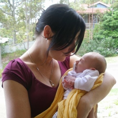 Catherine Rosser stands holding her baby in a yellow blanket