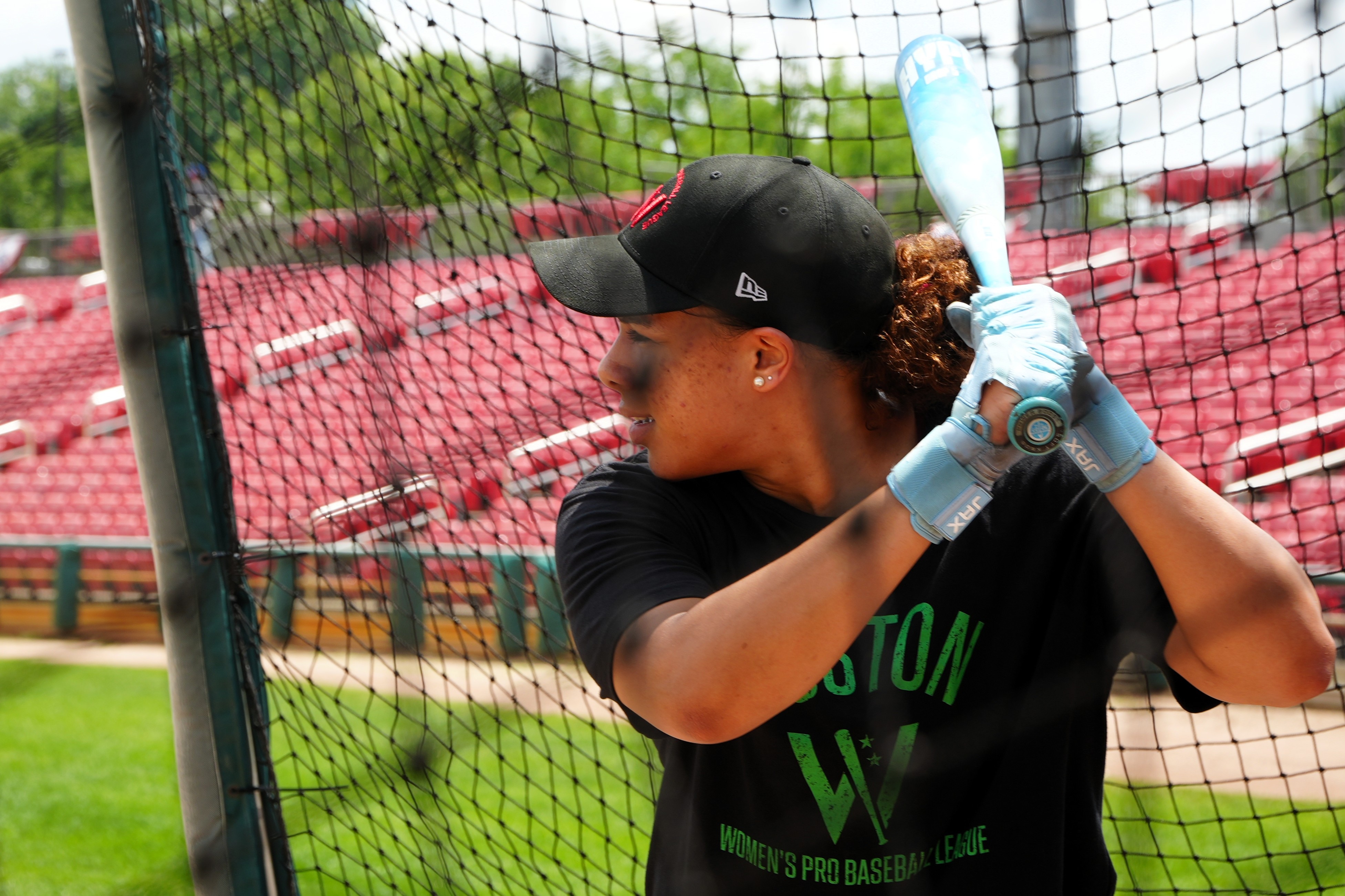 A female baseballer behind a net prepares to bat in practice
