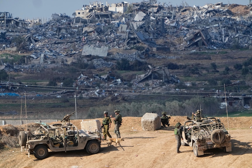  Israeli soldiers take up positions near the Gaza Strip border. Behind them are destroyed homes and buildings.