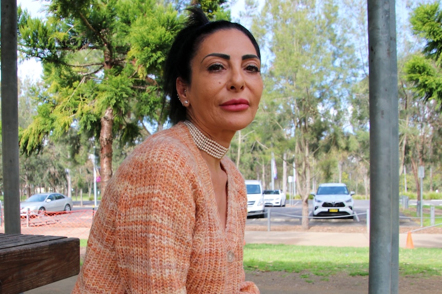 A woman sits outdoors near a carpark